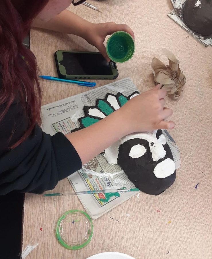 Freshman Savannah McMinn is painting part of her African cultural mask green in the fifth period class.