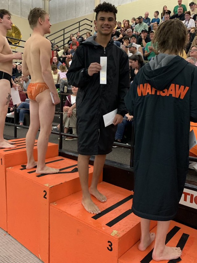 Sophomore Micah Rogers stands side by side with his opponents holding his third place ribbon at the Warsaw boys diving sectional. 