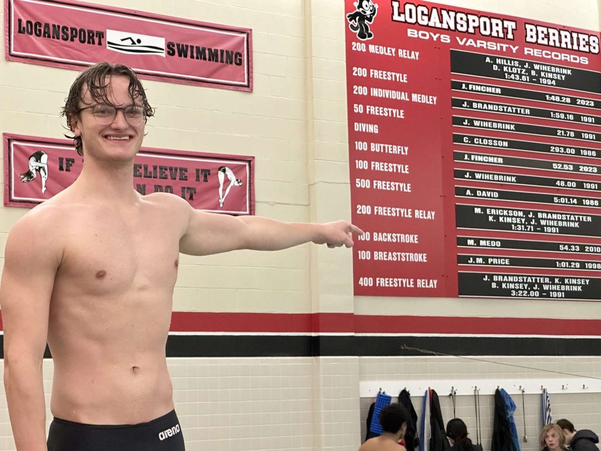 Senior Jake Fincher points at the record board after he broke the 100 backstroke record at the school. 