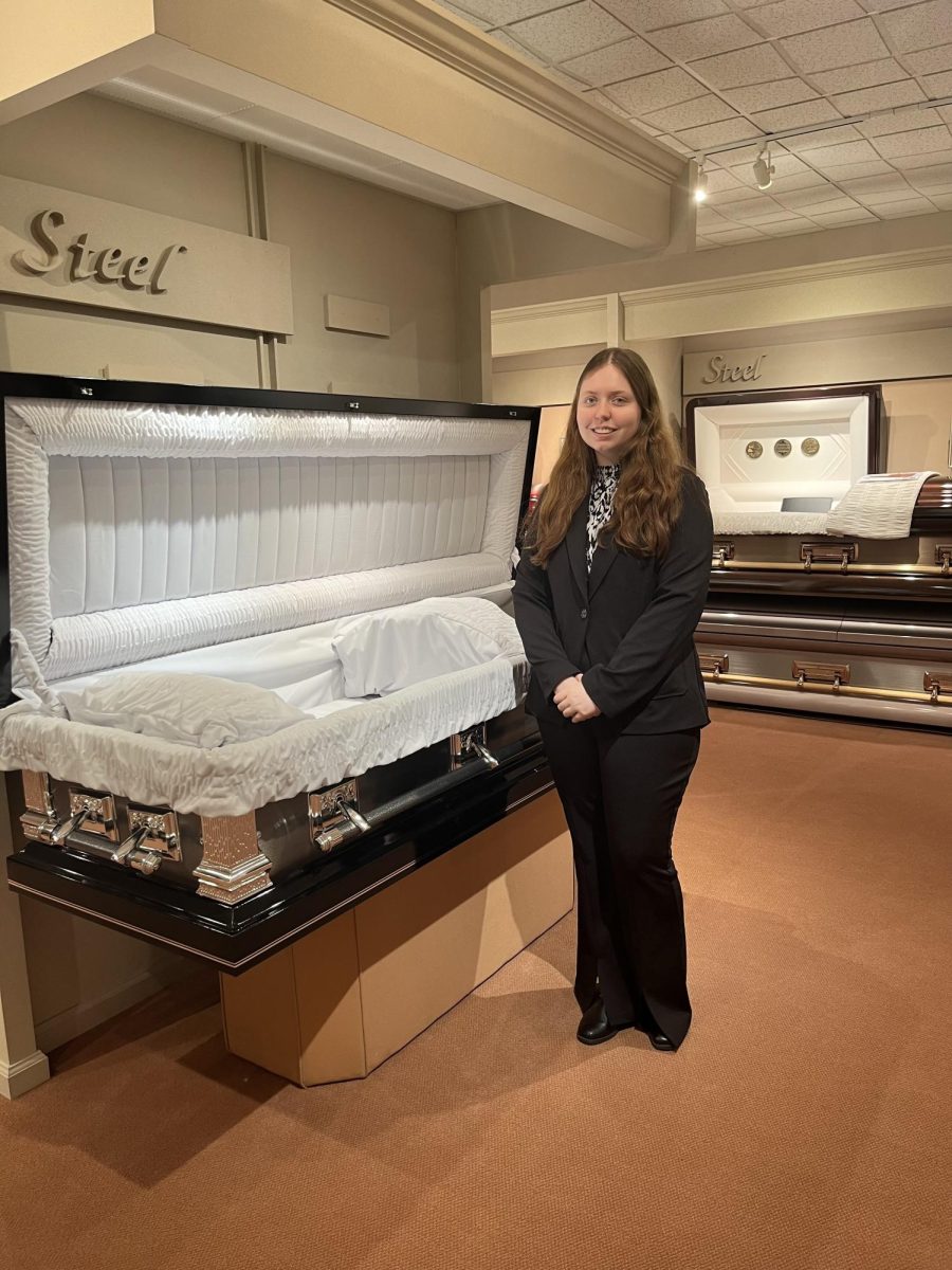 Standing next to a casket, senior Jaselyn Newbold is an intern at Fishers Funeral home working to become a funeral director. (Courtesy of Jaselyn Newbold)