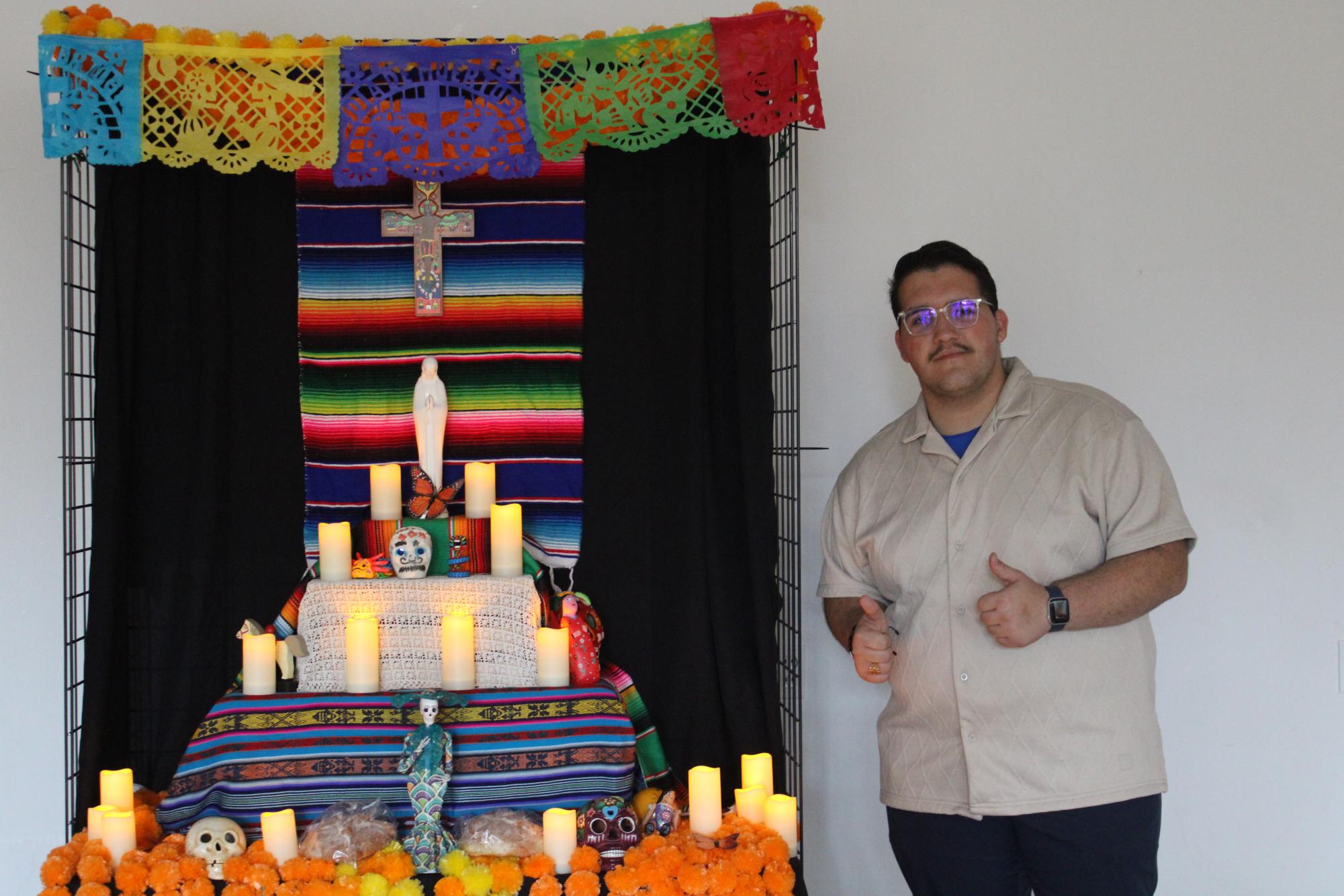 Posing, junior Yoslen Robaina Santana takes a picture with an ofrenda, a traditional altar set up to commemorate deceased loved ones.