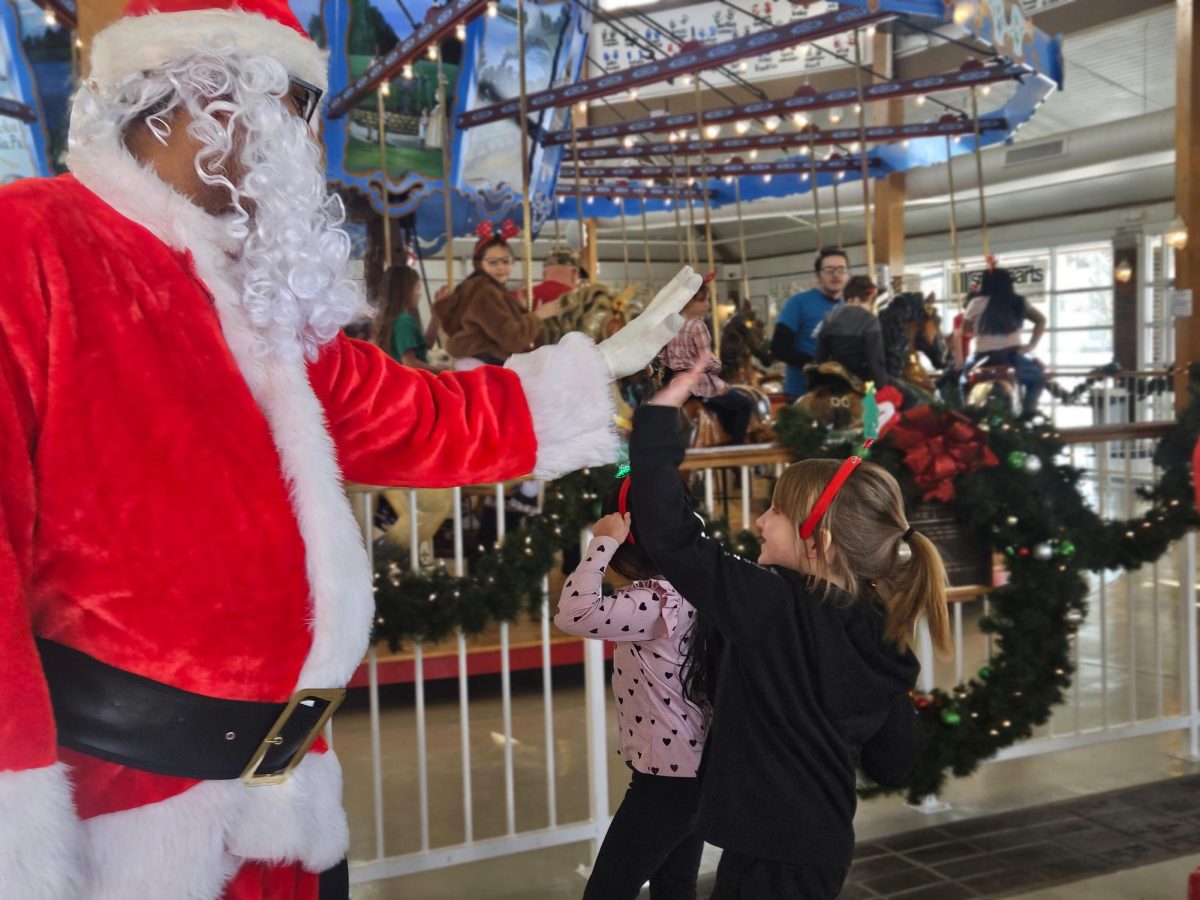 Entering the carousel, an elementary student is greeted by Santa Claus and high-fives him. Each kid received a festive headband as they arrived at the party. 
