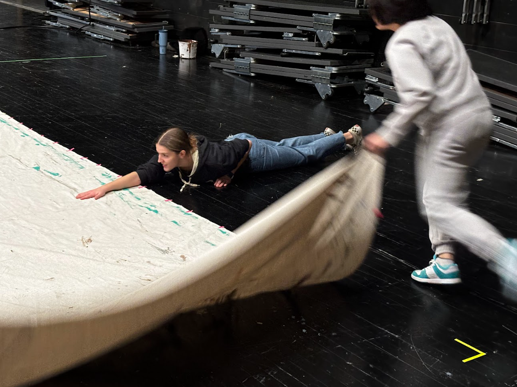 Ping lies on the floor, holding the cloth still, as Hsa prepares to jump over her.