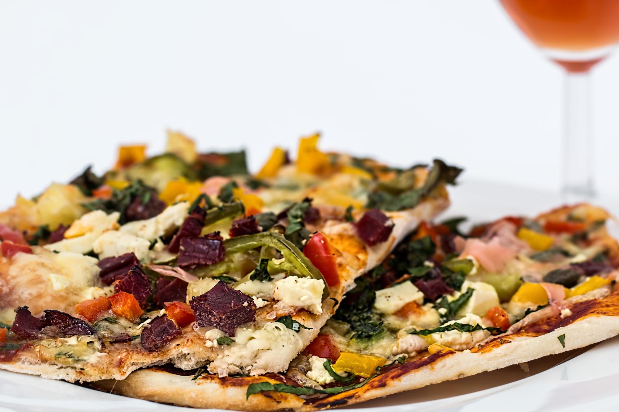 A vegetable flatbread pizza topped with feta cheese and colorful peppers sits on a white plate. (Pixabay)