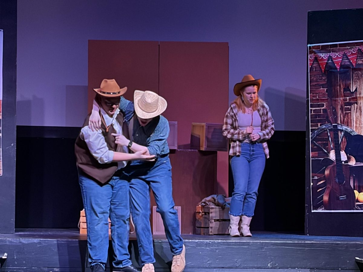 Sheriff Tickle (played by senior Calvin Mackey) is caught off guard by Milton (played by junior Chris Knapp) who just ran to him from the audience. The sheriff's daughter, Sarah (played by sophomore Molly Hunnicutt) watches the encounter with disgust.